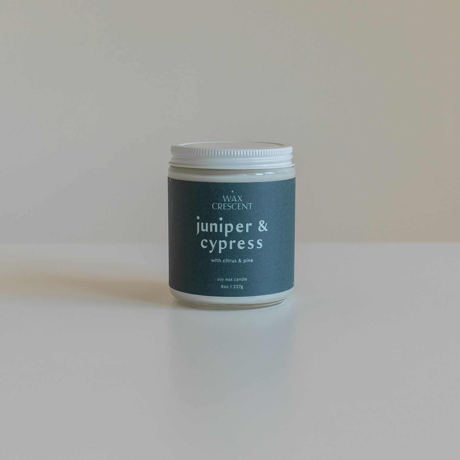 Unlit Juniper & Cypress candle with a deep blue label and white lid on a black background, emphasizing its elegant design and nature-inspired fragrance